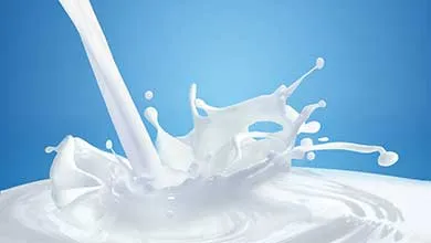 Milk stream splashes into a milk pool against a solid blue background.