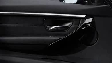 Close-up of a black car door interior featuring a polished chrome handle and integrated circular speaker.